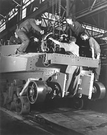 photographie en noir et blanc montrant des ouvriers guidant le moteur suspendu à une chaîne dans son emplacement