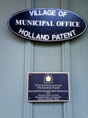 Plak pada Belanda Paten Stasiun Kereta api. Yang pertama berbunyi "Desa Holland Paten Kantor Kota." Yang kedua berbunyi "NYS Perlindungan Lingkungan Dana Holland Paten Depo Kereta api Restorasi, 2003. George E. Pataki, Gubernur; Bernadette Castro, Komisaris; Michael J. Bennison, Walikota."