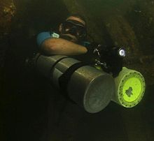 Sidemount diver partially removes (forward rotates) both primary cylinders to permit passage through a restriction in a wreck. Sidemount cylinder partial removal-crop.jpg