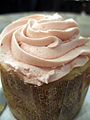 Cupcake with light pink frosting in brown paper wrapper.