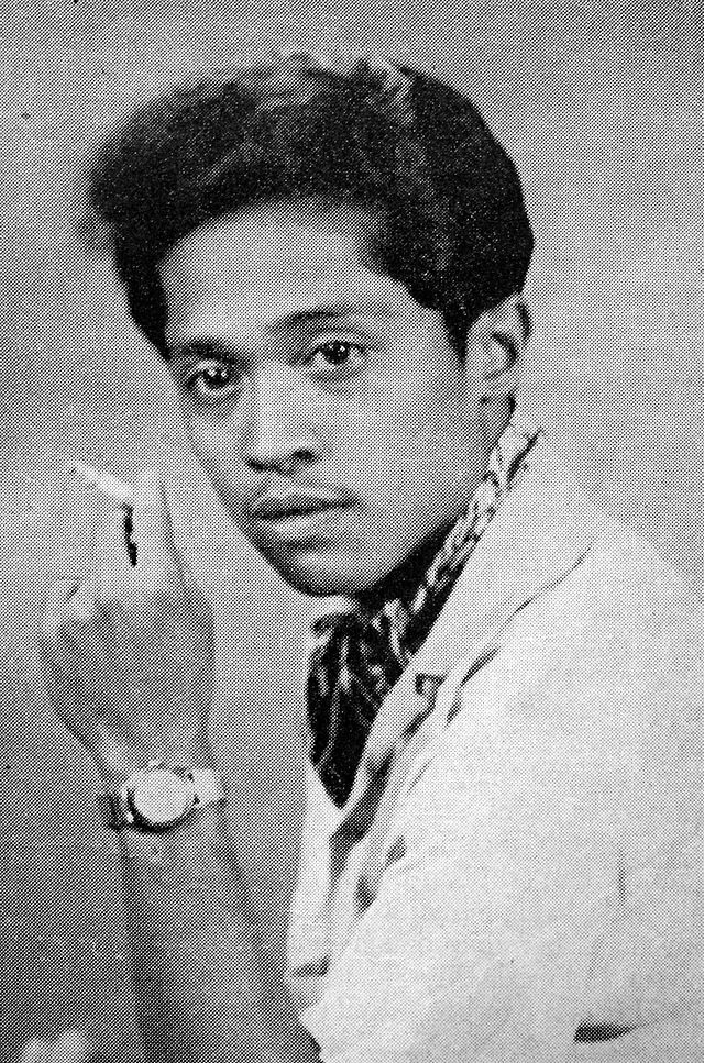 A man holding a cigarette, looking at the camera