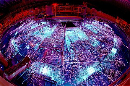 Overhead view from a fisheye lens of the Z machine at Sandia National Laboratory. Due to the extremely high voltage, the power feeding equipment is submerged in concentric chambers of 2 megalitres (2,000 m³) of transformer oil and 2.3 megalitres (2,300 m³) of deionized water, which act as insulators. Nevertheless, the electromagnetic pulse when the machine is discharged causes impressive lightning, referred to as a "flashover", which can be seen around many of the metallic objects in the machine.