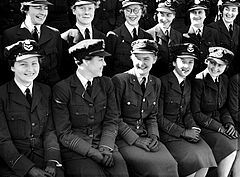 Svart-hvitt fotografi av sittende smilende kvinner kledd i mørke militæruniformer