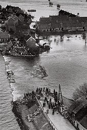 A breach in a levee in Papendrecht, the Netherlands, during the North Sea flood of 1953, flooding houses that had been built behind it Watersnoodramp 1953 dijkdoorbraak Papendrecht.jpg