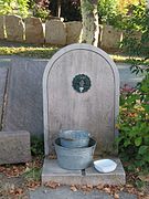 Photographie d’une fontaine au pied de laquelle des seaux sont posés.