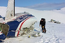 zerrissene Flugzeugstruktur, die auf Schnee steht, mit einem Mann, der daneben steht