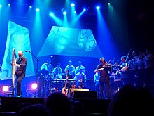 Foto van Alan op de harp, omringd door zijn pianist, zijn violist en de bagad van Saint-Malo