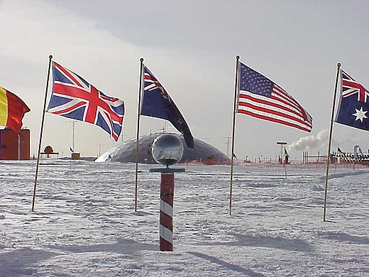 De zuidpool met het Zuidpoolstation, omringd met vlaggen van de landen die akkoord zijn gegaan met het Antarctisch Verdrag. In werkelijkheid beweegt de ijskap, en ligt de geografische pool een paar honderd meter buiten dit ceremoniële punt.