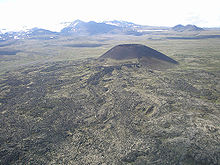 Terbuka berbentuk kerucut gunung naik di atas dataran tinggi dengan glaciated gunung yang menjulang di latar belakang.