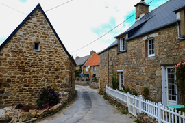 Photographie en couleurs prise à l'entrée d'une voie de circulation. De chaque côté, on voit des maisons construites en pierres apparentes, les toits sont recouverts d'ardoises ou de tuiles.