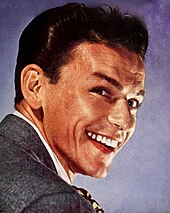 Close-up studiofoto van een jonge, lachende Sinatra met gestyled haar in een pak en stropdas