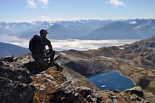 A hiker on the summit of Gentoo Peak, with upper Turnagain Arm in the background. Turnagain Arm is a largely silt-clogged fjord known for its extreme tides (including bore tides), treacherous silt flats, and population of beluga whales. Gentoo Peak. Chugach State Park, Alaska.jpg