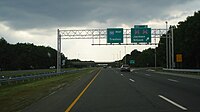 A four lane freeway at an interchange in a wooded area with two green signs over the road. The left one reads Interstate 195 west Trenton and the right one reads exit 21 County Route 527 County Route 526 Jackson Siloam upper right arrow