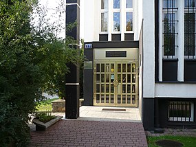 Przedstawia częściowo przeszklone i ze złotymi framugami drzwi wejściowe do Wypożyczalni Głównej i Czytelń w siedzibie głównej Miejskiej Biblioteki Publicznej im. Zofii Urbanowskiej w Koninie.