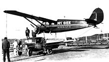 Foto hitam putih yang menunjukkan sebuah pesawat sedang diangkut di sebuah truk.