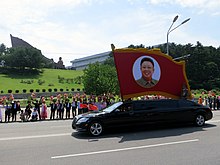 After the death of Kim Jong Il in 2011, every march past at North Korean military parades from 2012 to 2018 would have a black limousine carrying a red flag with Kim Jong Il's portrait following behind a black limousine carrying a red flag with his father Kim Il Sung's portrait. North Korea Victory Day 185 (9494850088).jpg