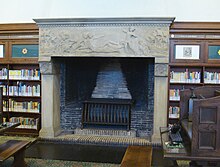 Photographie couleur d'une salle de lecture, avec la cheminée en gros plan et son manteau en pierre sculptée.