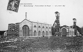 Photo noir et blanc un ensemble de bâtiments industriels typés 1900 avec deux grands chevalements (tour avec bigue) métalliques et cheminée d'usine.