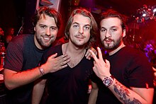 Three middle-aged Swedish men, all wearing black shirts, pose for a photograph during a DJ set.