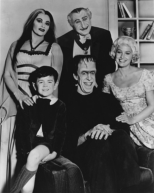 The cast of The Munsters in an early publicity photo. Standing, L–R: Yvonne De Carlo, Al Lewis. Sitting: Butch Patrick, Fred Gwynne, Beverley Owen