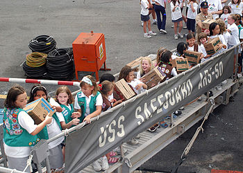 Girl Scout Brownies (right, brown vests) and Juniors (left, teal vests) at a charity event. US Navy 050509-N-4205W-002 Girl Scouts and Brownies from two troops in Singapore pass Girl Scout cookie boxes up the brow of the rescue and salvage ship USS Safeguard (ARS 50) as part of Operation Thin Mint.jpg