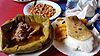 Traditional meal consisting of Sima/ Ugali (cooked white mealie meal) with Chapati (thin rounded roti), Matoke (mashed green bananas), sugar beans, mboga (green vegetables) and goat meat steamed in and served in a bowl wrapped around green banana leaves.