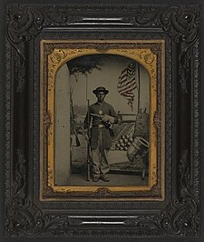 Portrait of African American Union soldier at Benton Barracks (Unidentified African American Union soldier with a rifle and revolver in front of painted backdrop showing weapons and American flag at Benton Barracks, Saint Louis, Missouri) (LOC) (5229147154).jpg
