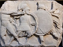 Dos guerreros entrechocan sus escudos mientras que a su izquierda, un arquero mira su blanco