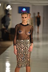 A see-through top worn along with pasties by a model at a fashion show in US, 2017. Such fashion trends get popularised through media. Crystal Couture Fashion Show & Sale (32801142162).jpg