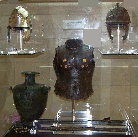 Hoplite armour exhibit from the Archaeological Museum of Corfu. Note the gold inserts around the chest area of the iron breastplate at the centre of the exhibit. The helmet on the upper left is a restored version of the oxidised helmet on the right.