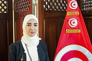Visage d'une femme voilée à gauche d'un drapeau tunisien.