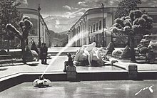 photographie en noir et blanc d'une fontaine et d'une statue, avec des montagnes en arrière plan.