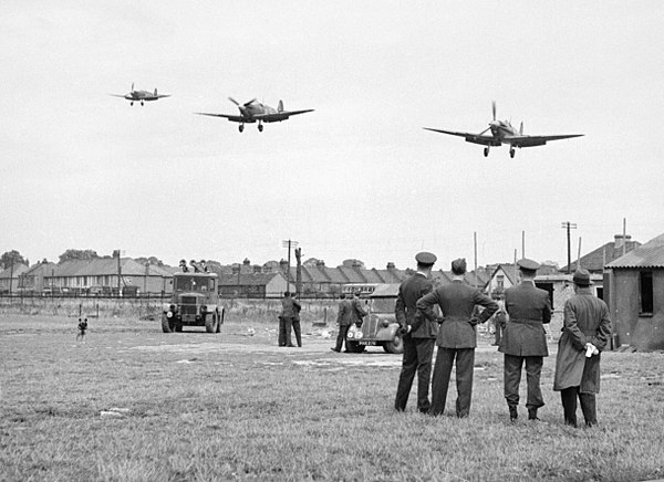 Personnel of No. 121 Squadron look on as three Spitfire Vbs come in to land at RAF Rochford in Essex, after a fighter sweep over northern France durin