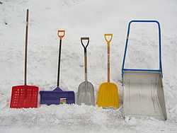 雪が積もった地面に並ぶ雪かき道具の写真。金属製およびプラスチック製のスコップなど4点の右にアルミ製のスノーダンプ。