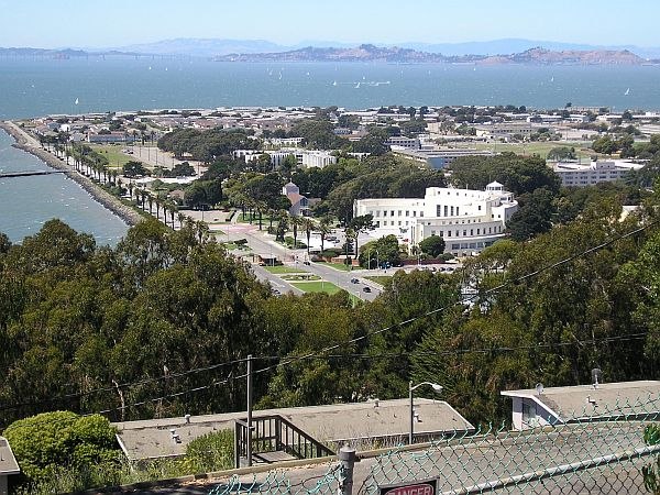 Treasure Island beyond Yerba Buena Island's rooftops and trees, which obscure the causeway and marina. The large curved white building (right of cente