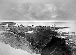 Photographie en noir et blanc d'un village sur un éperon rocheux au bord d'un lac.