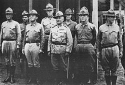 Eight people in military uniforms. They are wearing hats and are standing in formation.