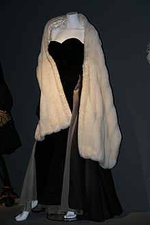 Robe noire décolletée et large étole blanche en fourrure exposées sur un mannequin en plastique