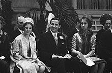 Fotografía que muestra a tres personas sentadas: un hombre con traje de tres piezas y dos mujeres, una con abrigo ligero y turbante y la otra con abrigo bordado, gorro y bufanda de piel.