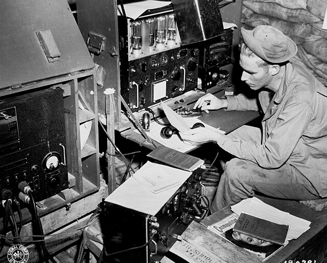 Radio operator Cpl. John Robbins, 41st Signal, 41st Infantry Division, operating his SCR 188 in a sandbagged hut at Station NYU. Dobodura, New Guinea 