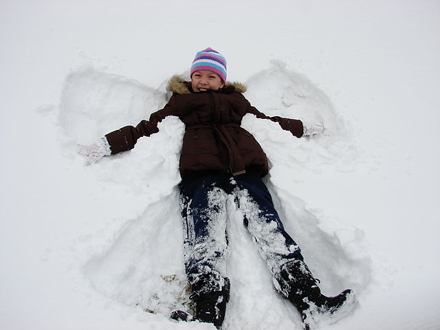 On The Snow Is A Child In The Pose Of The Angel. Hands Spread Out In  Different Directions. Waving His Arms Like Wings. Sunny Day. Pure Snow.  Winter Vacation On Vacation Or