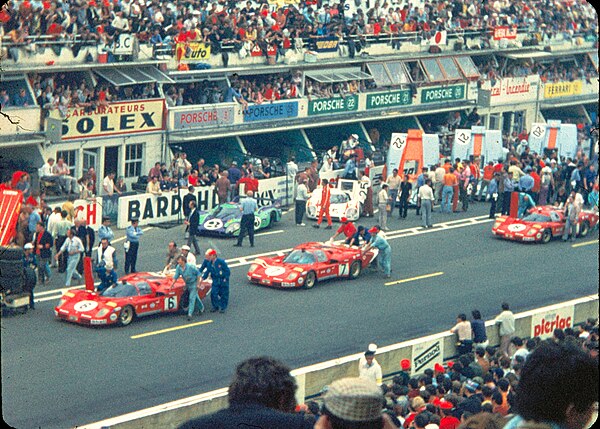 Cars being arranged at the start line before the race. Three Scuderia Ferrari 512 S are visible in the foreground, with the six Porsche 917s of Gulf, 