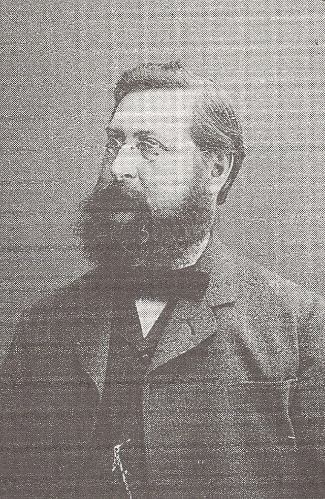 Porträtfoto von Heinrich Züge aus dem Jahr 1885. Zu sehen ist ein Mann mit Vollbart und Brille von der Brust aufwärts, links am Betrachter vorbei blickend.