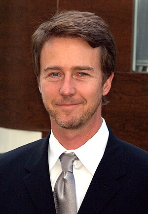 A portrait of Edward Norton, a blonde Caucasian man in a white plaid shirt. He is smiling towards the camera