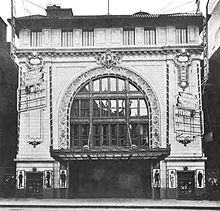 Черно-белое фото театра со сводчатым потолком и богато украшенным занавесом перед сценой.