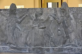 God Ea (Sumerian Enki), flanked by fish-cloaked apkallus, part of a basalt water basin from Assur, Iraq. Reign of Sennacherib, 7th century BCE. Pergamon Museum.jpg