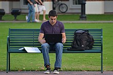 A man using a laptop on a park bench Homework (8120708019).jpg