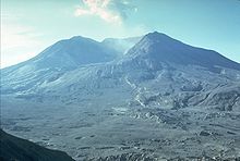 前の写真と同じ位置からみた噴火後の山容。山体の多くが失われ、巨大なカルデラ（火口）が生じている。以前森林に覆われていた景観は、火山の爆発で破壊され、未だ荒野が広がっている。