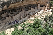 um grupo de pessoas observando ruínas indígenas localizadas em uma caverna.