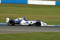 Carro branco e azul, vista de perfil, em uma pista.